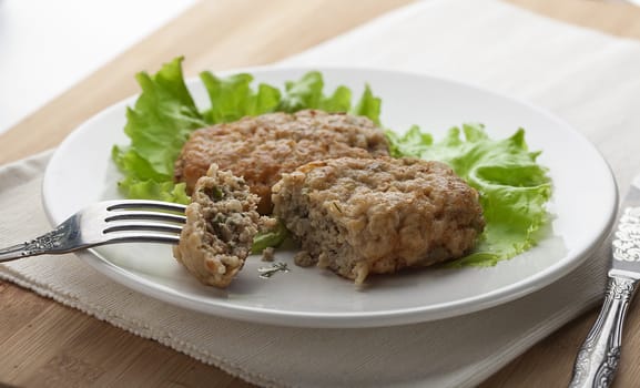 White plate with two rissoles and green lettuce on the napkin on the wooden board