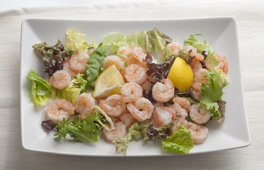 Boiled shrimp's tails with lemon and lettuce on the white plate