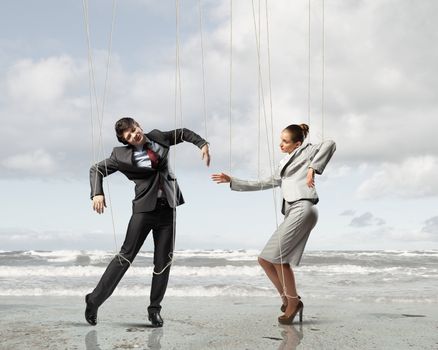 Image of businesspeople hanging on strings like marionettes against sea background. Conceptual photography