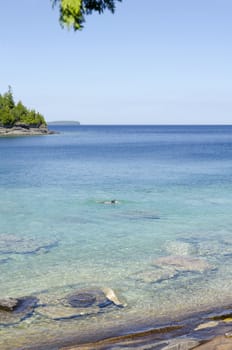 Green and blue water of Huron Lake, Ontario under blue sky.