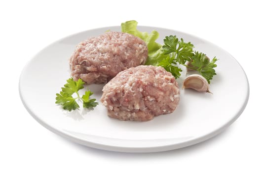 Two raw chicken rissoles with parsley, garlic and lettuce on the white plate