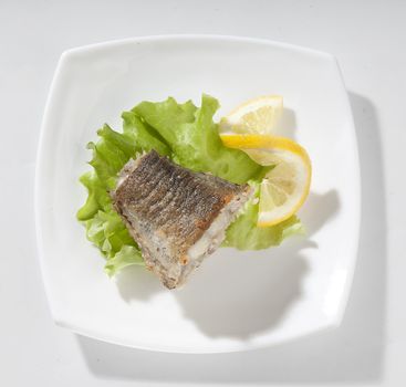 Fried piece of cod with lettuce and lemon on the plate