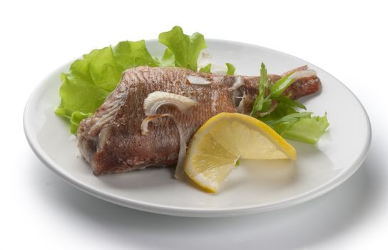 Baked rosefish with lettuce and lemon on the plate
