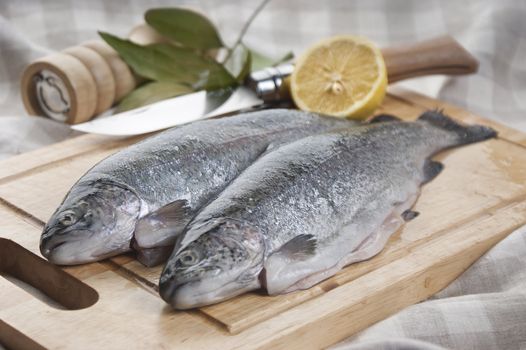 Two raw trunks of rainbow trout on the wooden board with lemon and bay leaf