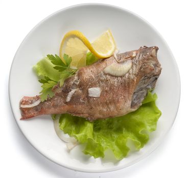 Baked rosefish with lettuce and lemon on the plate