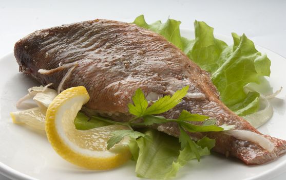 Baked rosefish with lettuce and lemon on the plate