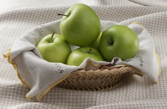 Some green apples in the wicker on the tablecloth