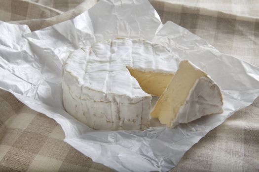 Camembert cheese in the white paper on the tablecloth