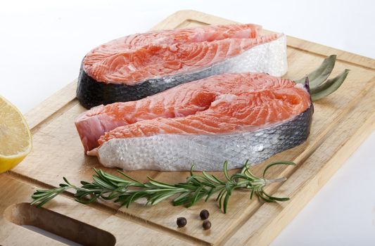 Two raw steak of salmon with rosemary, pepper, bay leaf and lemon on the wooden board