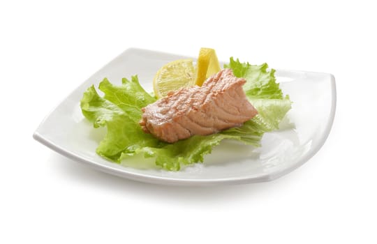 Piece of steamed salmon with lemon and lettuce on the white plate