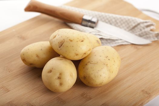 Some raw potatoes on the wooden board with knife