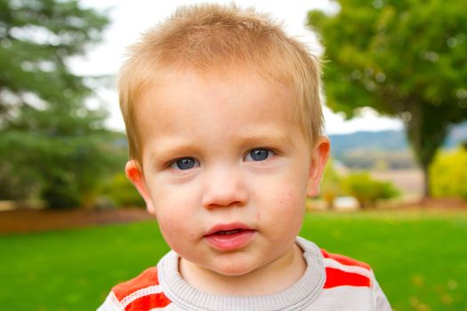 A portrait of a young boy playing outdoors wearing a red and white striped shirt.