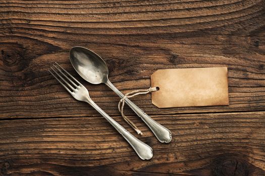Old fork and spoon with paper label on wooden background