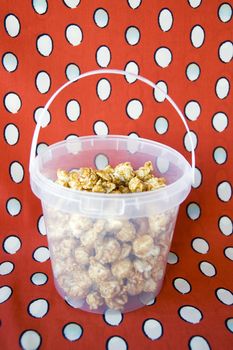 caramel popcorn in plastic bucket on red background