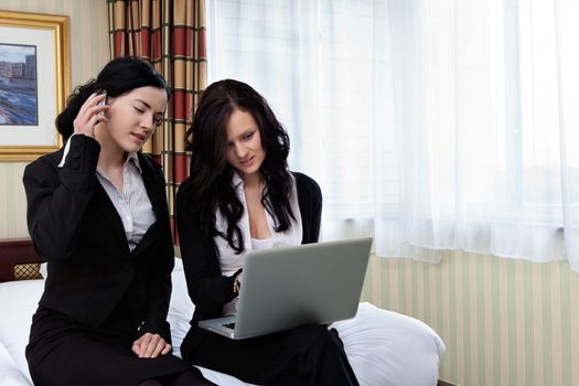 Female executive working on laptop while her colleague talks on cell phone