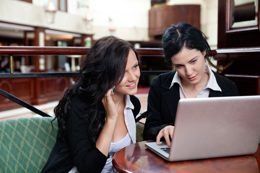 Female executive working on laptop while her colleague talking on cell phone