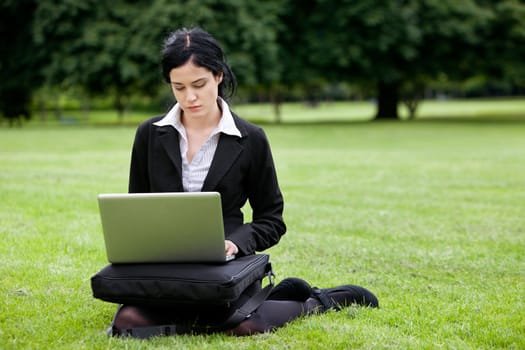 Young attractive businesswoman sitting in park working on laptop