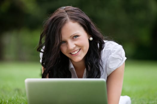 Close-up portrait of pretty female lying on grass using laptop