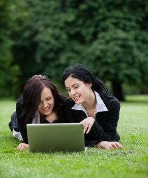 Two young business stuents in park with laptop