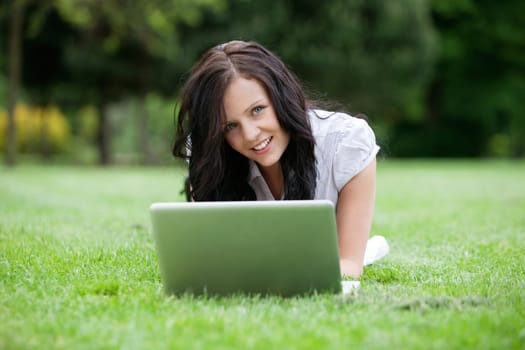 Portrait of attractive female lying on grass using laptop
