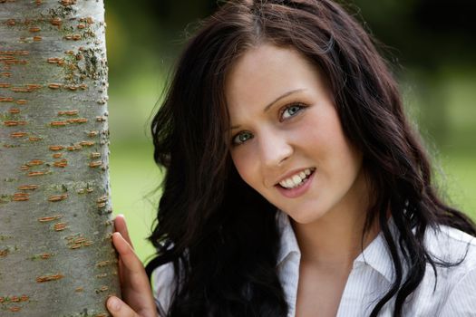 Portrait of cute smiling female standing near tree trunk