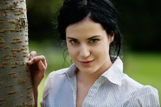 Portrait of beautiful smiling female standing near tree trunk