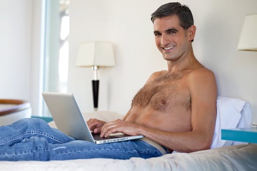 Portrait of smiling shirtless middle aged man working on laptop