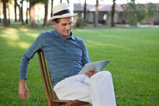 Relaxed casual man sitting in park using tablet PC