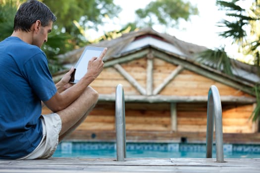 Casual man holding tablet PC while sitting at swimming pool's edge