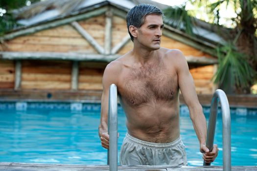 Handsome man coming out of the swimming pool and looking away