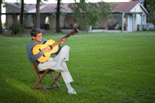Full length of casual relaxed middle aged man playing guitar in the lawn