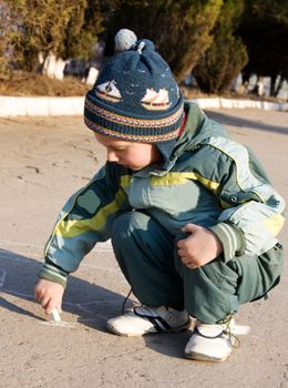 Kid playing on the ground with chalk.