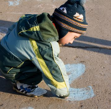 Kid playing on the ground with chalk.