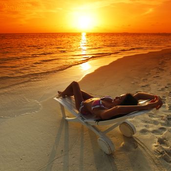 Woman in chaise-lounge relaxing on sunset beach