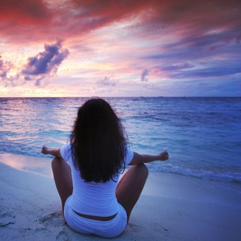 Yoga woman in lotus pose on beach at sunset