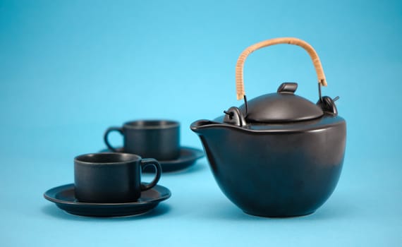 retro ceramic black teapot and small cups in saucers composition on blue background.