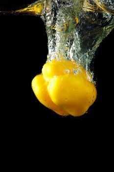 Colored yellow paprika in water splashes on black background