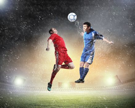 two football players in jump to strike the ball at the stadium