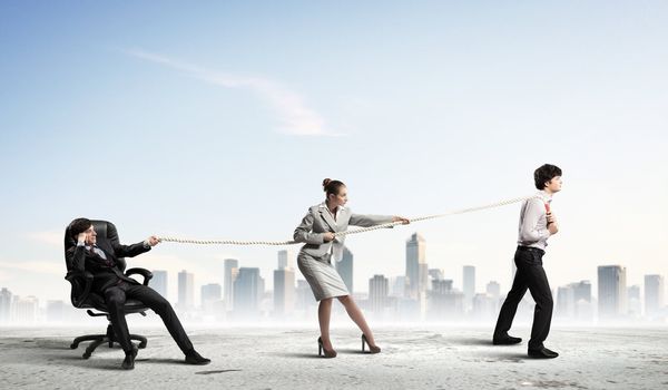 Image of three businesspeople pulling rope against city background