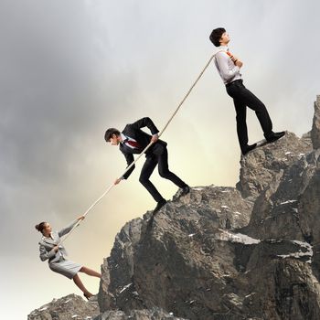 Image of three businesspeople pulling rope atop of mountain