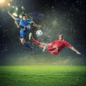 two football players in jump to strike the ball at the stadium