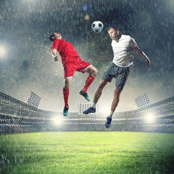 two football players in jump to strike the ball at the stadium