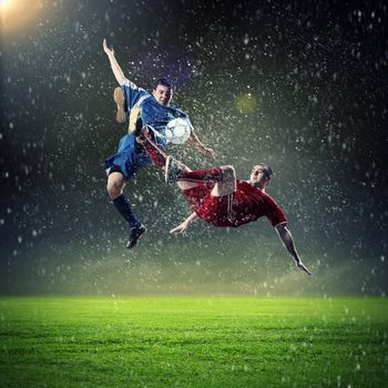 two football players in jump to strike the ball at the stadium