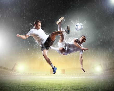 two football players in jump to strike the ball at the stadium