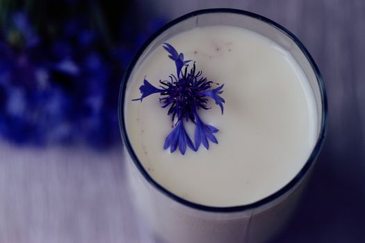 glass of milk and a bouquet of cornflowers on a purple table