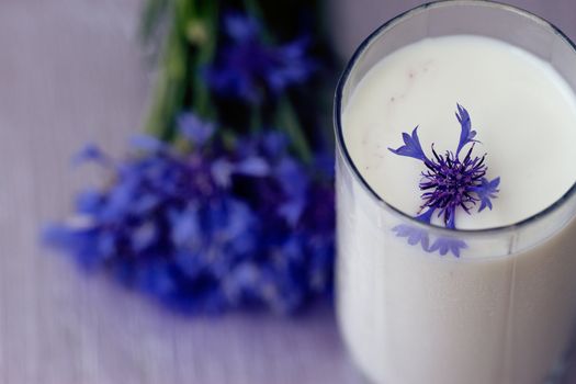 glass of milk and a bouquet of cornflowers on a purple table