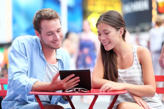 Multiethnic couple dating in New York City on Times Square. Man showing woman tablet pc smiling happy together.