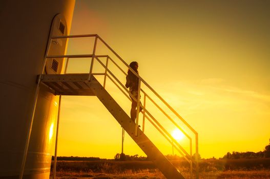 Girl standing on a stairs to windturbine during amazing sunset