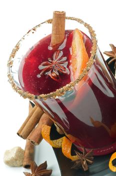 Glass of Mulled Wine and Spices with Cinnamon Stick, Orange, Anise Star and Sugar on Black Saucer closeup on white background