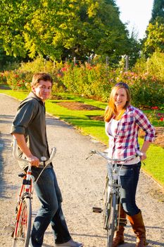 A man and a woman with their bicycles on a bike path in an outdoor park setting.